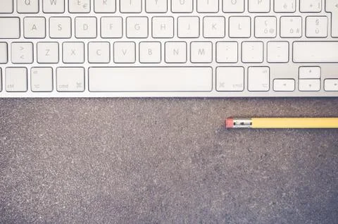 A top view closeup of a computer keyboard and a yellow pencil on a stone text Stockfoto's