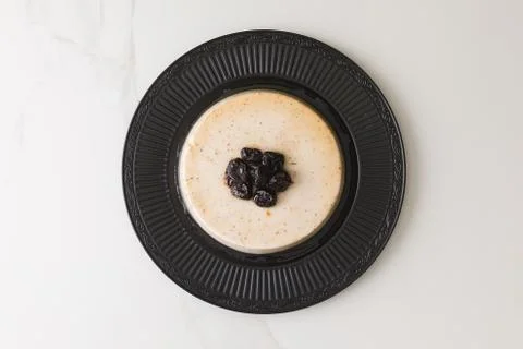Top view of a coconut pudding with plums in a black plate in a marble table a 写真素材