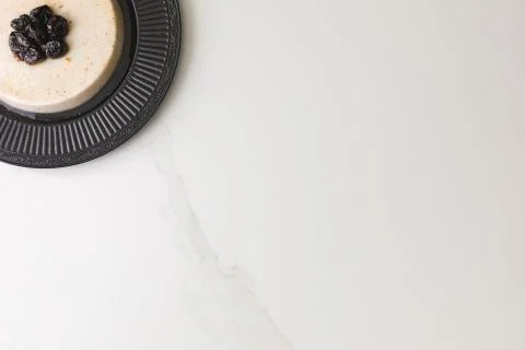 Top view of a coconut pudding with plums in a black plate in a marble table a 写真素材
