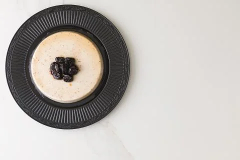 Top view of a coconut pudding with plums in a black plate in a marble table a Stock Photos