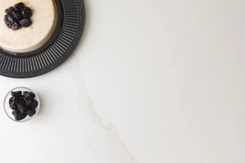 Top view of a coconut pudding with plums in a black plate in a marble table w 写真素材