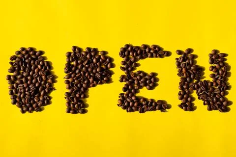 Top view of coffee beans in the form of letters reading "open" on yellow back Stock Photos