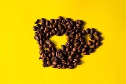 Top view of coffee beans in the shape of a cup with heart in the center on ye Stock Photos