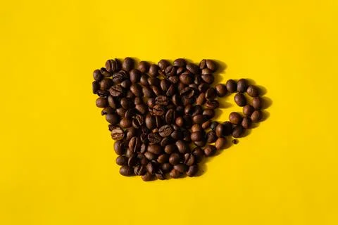 Top view of coffee beans in the shape of a cup on a yellow background. Stock Photos