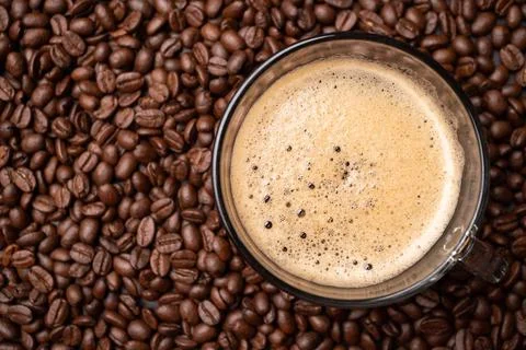 The top view of a coffee cup and group of black coffee beans is the backgroun Stock Photos