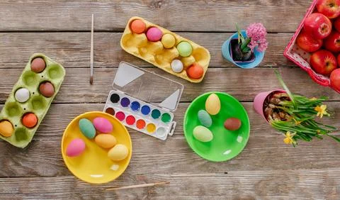 Top view of colorful Easter eggs, paints and brushes on wooden table with flo Stock Photos