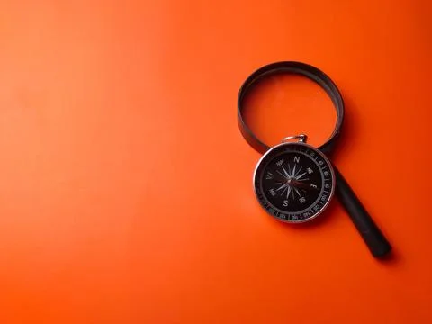 Top view compass and magnifying glass on a orange background Stock Photos