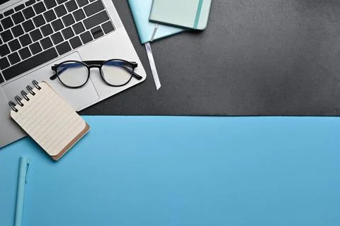 Top view computer tablet, eyeglasses and notebook on blue and black background. Stock Photos