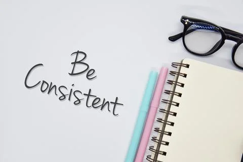 Top view concept of notebook, pens and spectacle with word 'Be consistent' Foto stock