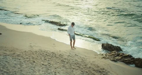 Top view of a confident brunette guy in a white shirt and shorts walking along Stock Footage 283834243