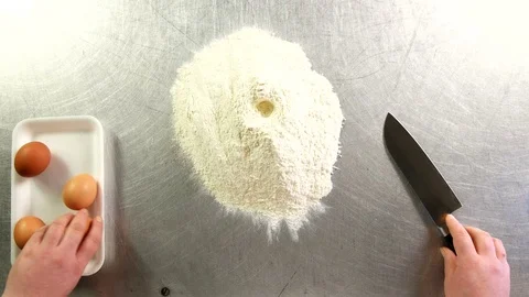 Top view the cook breaks the egg with a knife and throws it into the flour Stock Footage 76123131
