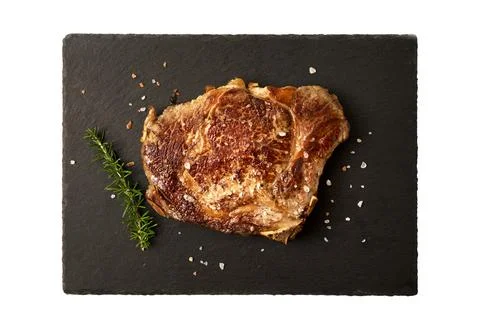 Top view cooked beef steak on dark cutting board with salt and rosemary. Stock Photos