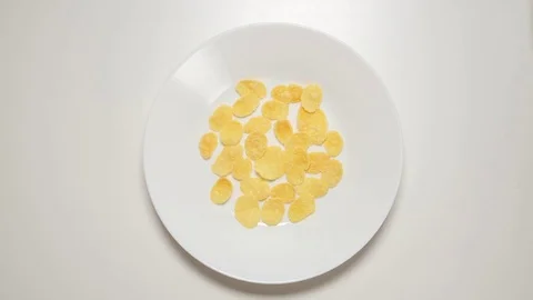 TOP VIEW: Corn flakes appear on a white dish on a white table (stop motion) Video stock 69809443