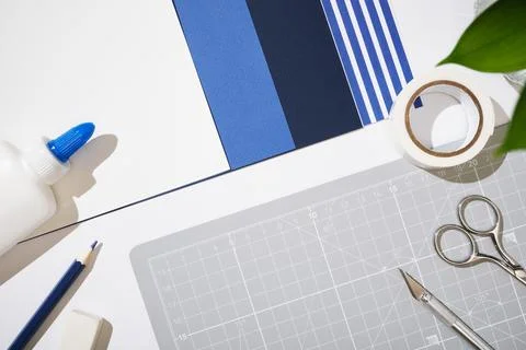 Top view of crafting tools on a grey cutting mat with blue paper samples. C.. 스톡 사진