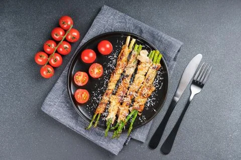 Top view of crispy bacon wrapped asparagus with cherry tomatoes on black pl.. Foto stock