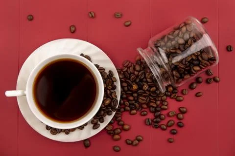Top view of a cup of coffee with coffee beans falling out of a glass jar on.. Stock Photos
