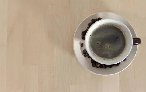 A top view of a cup of coffee with some coffee beans on the plate, over a w.. 스톡 사진