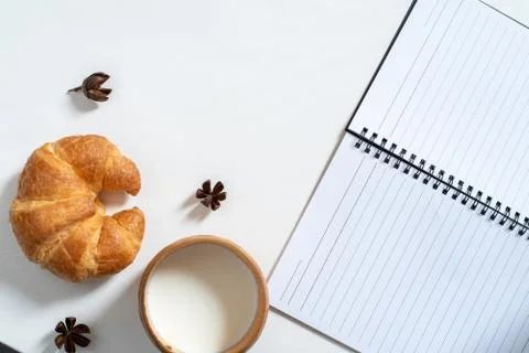 Top view of cup of milk, note book, croissant on wooden table Stock Photos