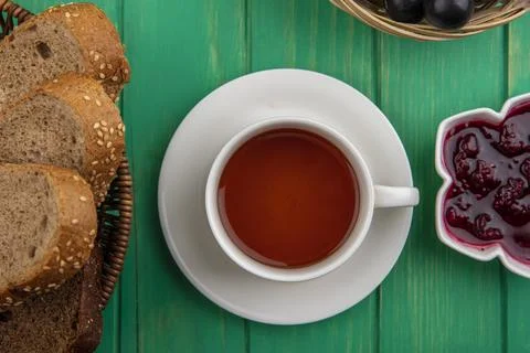 Top view of cup of tea with seeded brown cob slices and raspberry jam on gr.. Stock Photos