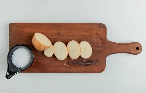 Top view of cut and sliced potato and salt on cutting board on white backgrou Stock Photos