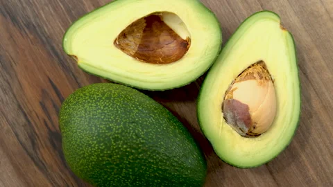 Top view of cut avocado fruit rotating on a wooden surface Stock Footage 272226916