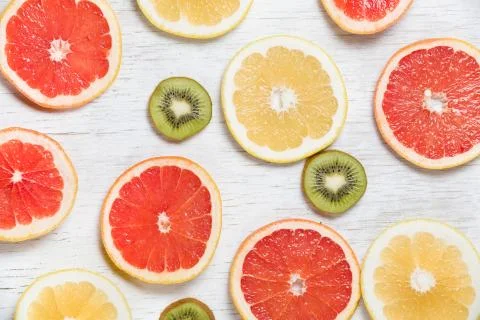 Top view on cut red and yellow grapefruit and kiwi on white wooden background Stock Photos