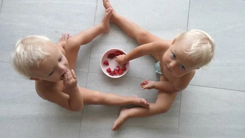 Top view of cute twins sitting on the floor eating strawberries from shared cup Video stock 154166064