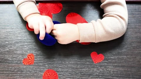 Top view of cutted red heart shapes and kid's hands playing with golden rings on Stock Footage 232023493