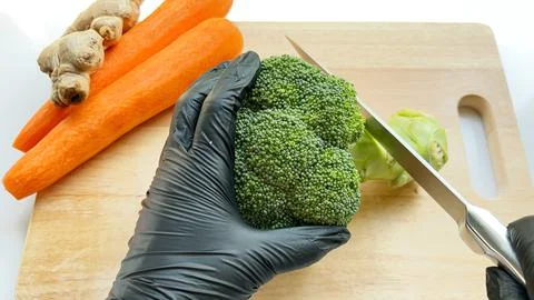 Top view of cutting fresh broccoli stem with sharp knife on the wooden board. Stock Photos