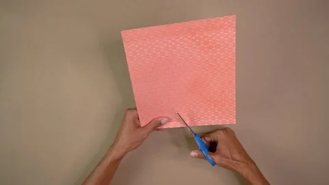 Top view of dark-skinned hands cutting pink patterned cardstock with scissors Stock Footage 344458877