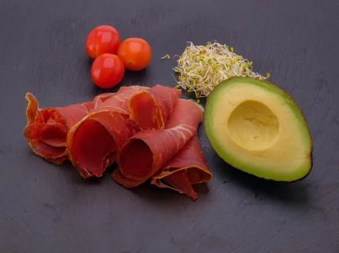 Top view on dark stone table with jamon , cherry tomatoes, avocado. Stock Photos