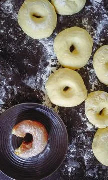 A top view of a dark surface covered in flour, with several uncooked doughnuts Stock Photos