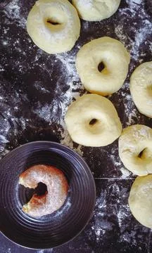 A top view of a dark surface covered in flour, with several uncooked doughnuts Stock Photos