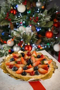 Top view of Delicious looking cake with fruits on top, behind a christmas tre Stock Photos