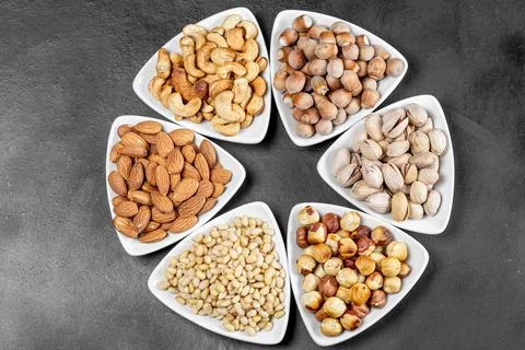 Top view, different nuts in white triangular bowls on a black background Stock Photos