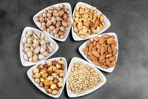 Top view, different nuts in white triangular bowls on a black background Stock Photos