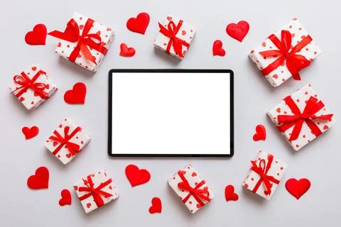 Top view of digital tablet with gift boxes and hearts on colorful background. Stock Photos