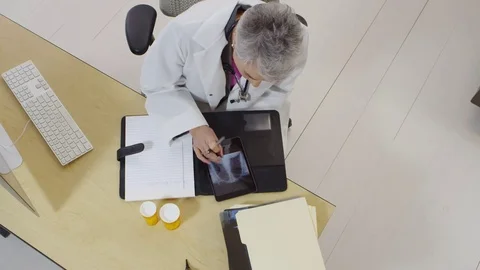 Top view of doctor looking at x-rays and taking notes on her tablet Video stock 80129238