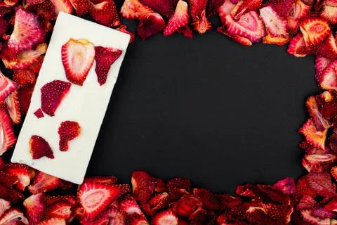 Top view of dried strawberry slices with white chocolate bar on black backg.. Stock Photos