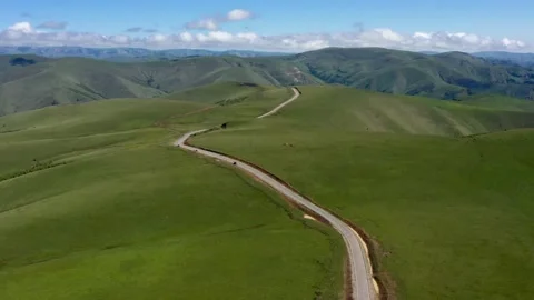Top view on the driving car of the mountain road through the green field. Drone Stock Footage 166063905