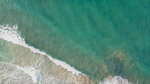 Top view drone shot of emerald green sea water surface with white foam wave.. Stock Photos