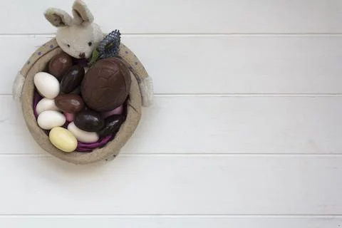 Top view of Easter Bunny basket with chocolate almond eggs on white wooden ta Stock Photos