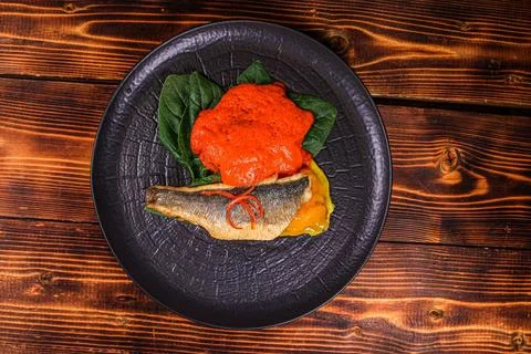 Top View: Elegant plating of pan-fried fish with red sauce on dark plate Stock Photos