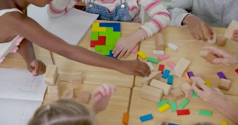 Top view of elementary pupil group sorting colorful blocks on wooden desk with Stock Footage 337465336