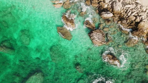 Top view of emerald green sea with rocks under clear shallow water lapping in Stock-Footage 327614937