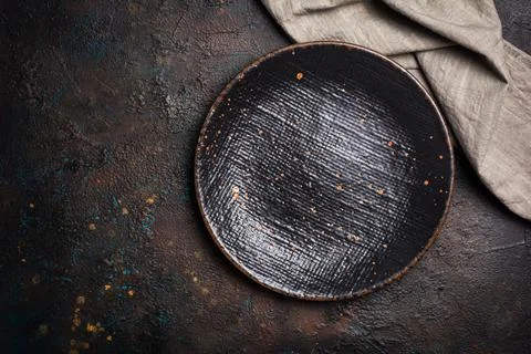 Top view of empty black ceramic plate with linen napkin on dark brown concret Stock Photos