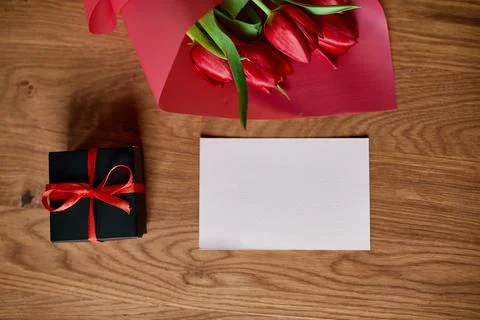Top view empty card with  red tulips flowers in red paper wrapper with gift b Stock Photos