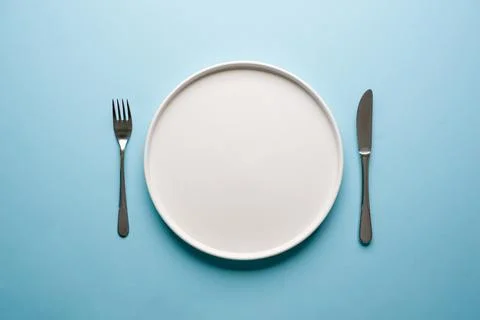 Top view of empty ceramic white plate and cutlery on blue background Stock Photos