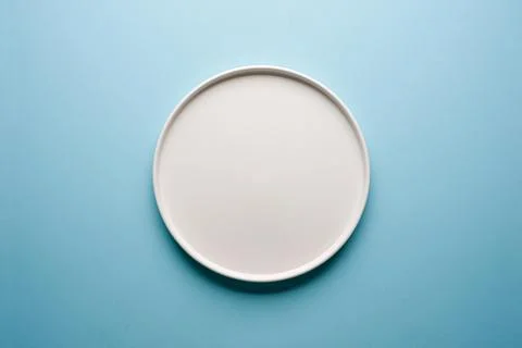 Top view of empty ceramic white plate on blue background Stock Photos