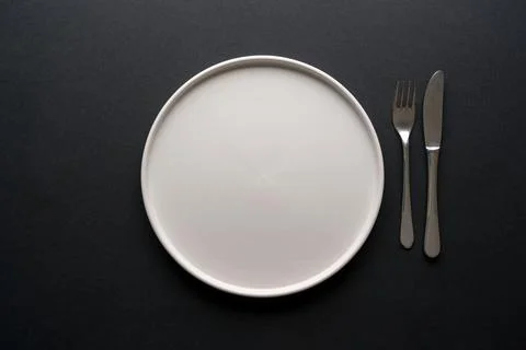 Top view of empty ceramic white plate and cutlery on black background Stock Photos